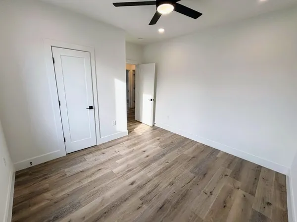 an empty room with wooden floor fan and windows