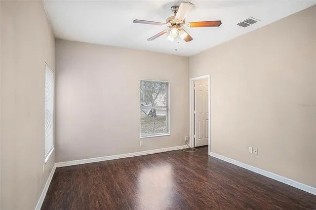 an empty room with wooden floor chandelier fan and windows