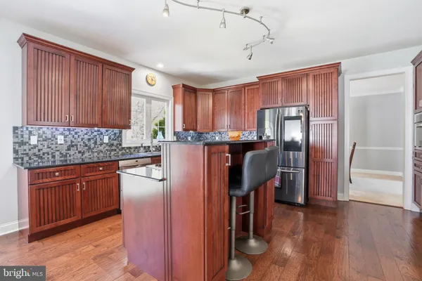 a kitchen with stainless steel appliances granite countertop wooden cabinets a refrigerator a stove a sink and dishwasher with wooden floor