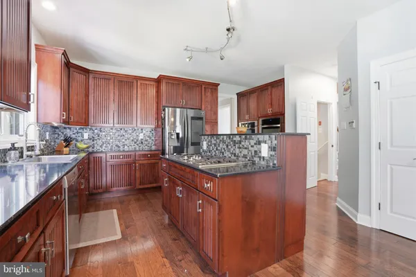 a kitchen with stainless steel appliances granite countertop a stove a refrigerator a sink dishwasher and wooden cabinets with wooden floor