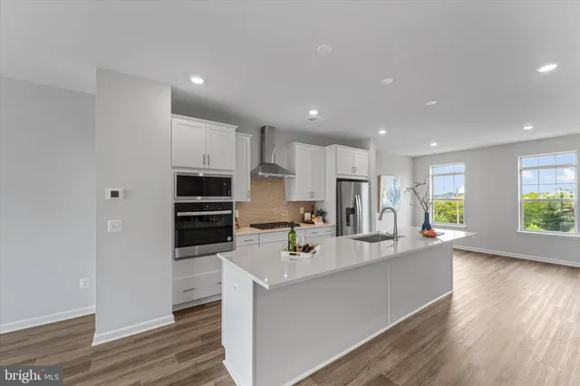 a large kitchen with stainless steel appliances kitchen island granite countertop a stove a sink a refrigerator and white cabinets with wooden floor