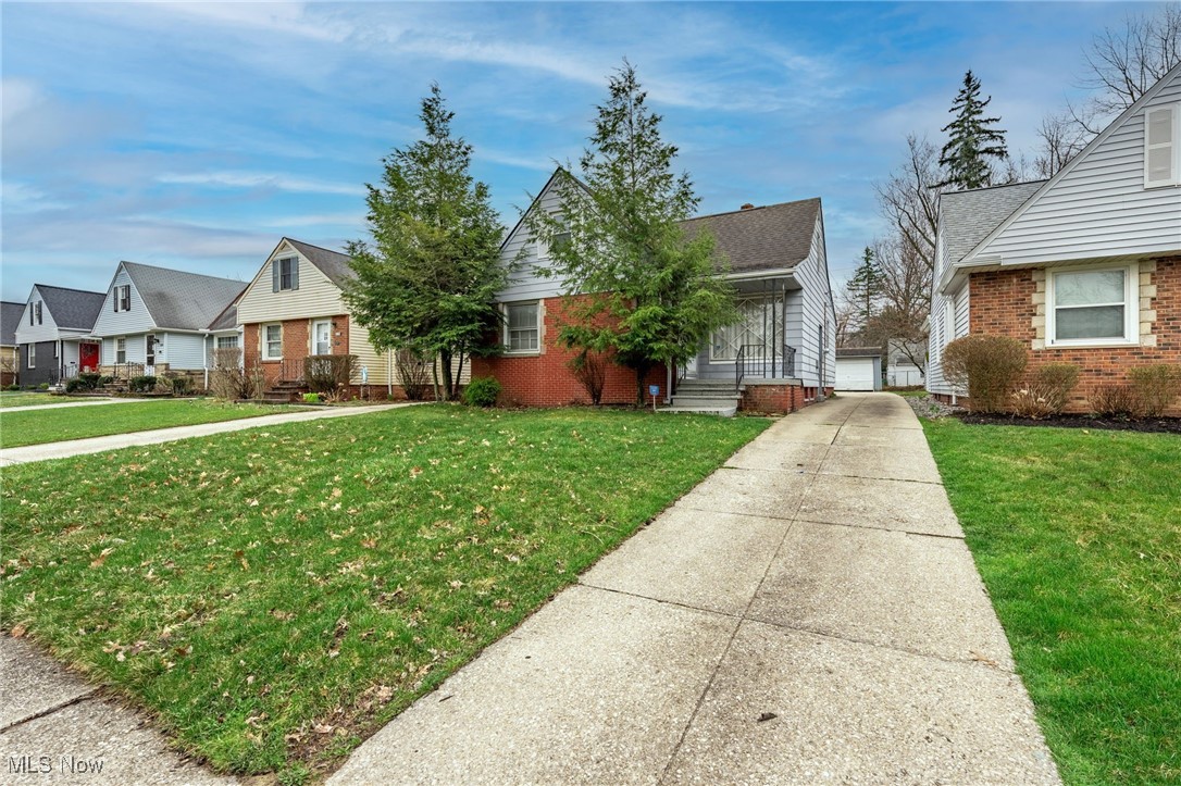 View of front of home with an outdoor structure, a residential view, brick siding, and a front yard