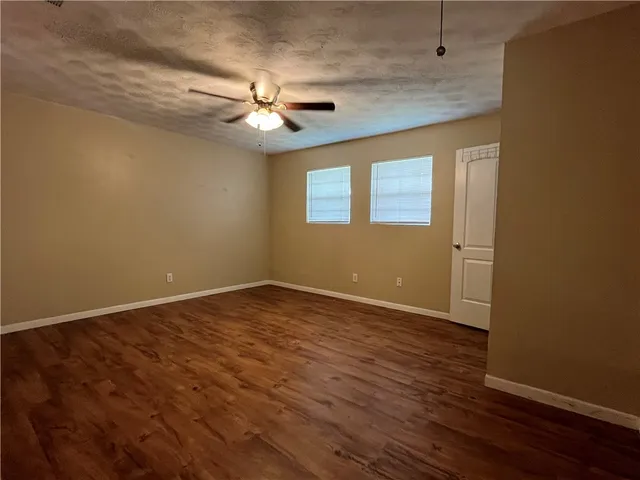 an empty room with wooden floor fan and windows