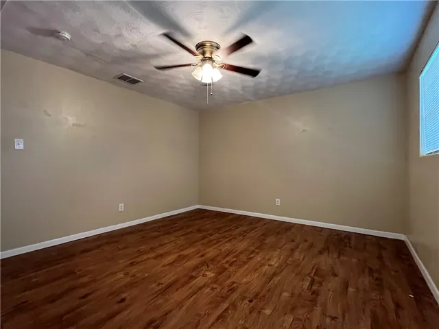an empty room with wooden floor fan and windows