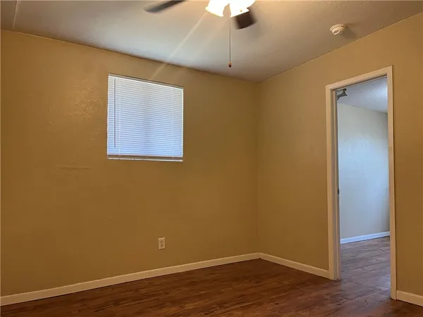 a view of an empty room with wooden floor and a ceiling fan