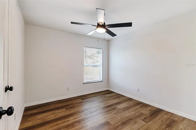 an empty room with wooden floor ceiling fan and windows