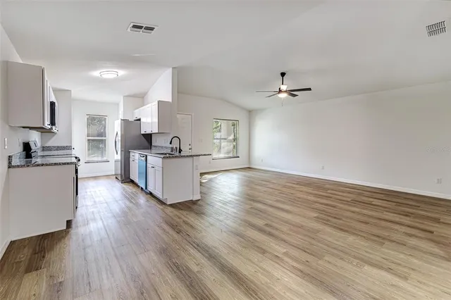 a kitchen with stainless steel appliances a refrigerator a sink dishwasher a stove and white cabinets with wooden floor