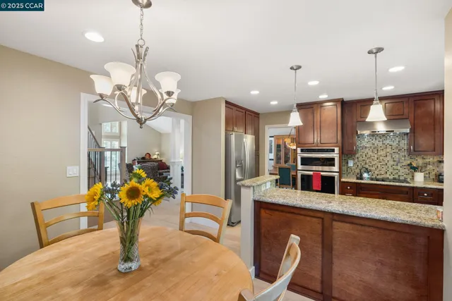 a kitchen with stainless steel appliances granite countertop a sink a stove a dining table chairs and chandelier