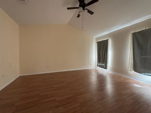 a view of an empty room with wooden floor and a ceiling fan