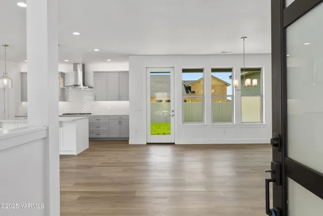 a view of an empty room with wooden floor and kitchen