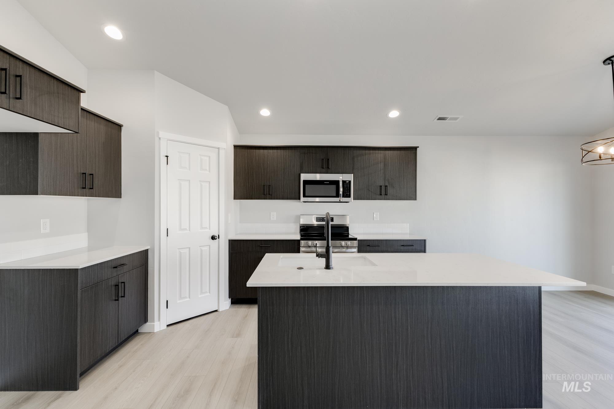 1804 West Unforgettable Street Meridian, ID 83642 - Photo 3 of 18 Kitchen with a kitchen island with sink, light stone countertops, stainless steel appliances, light wood-style floors, and dark brown cabinetry