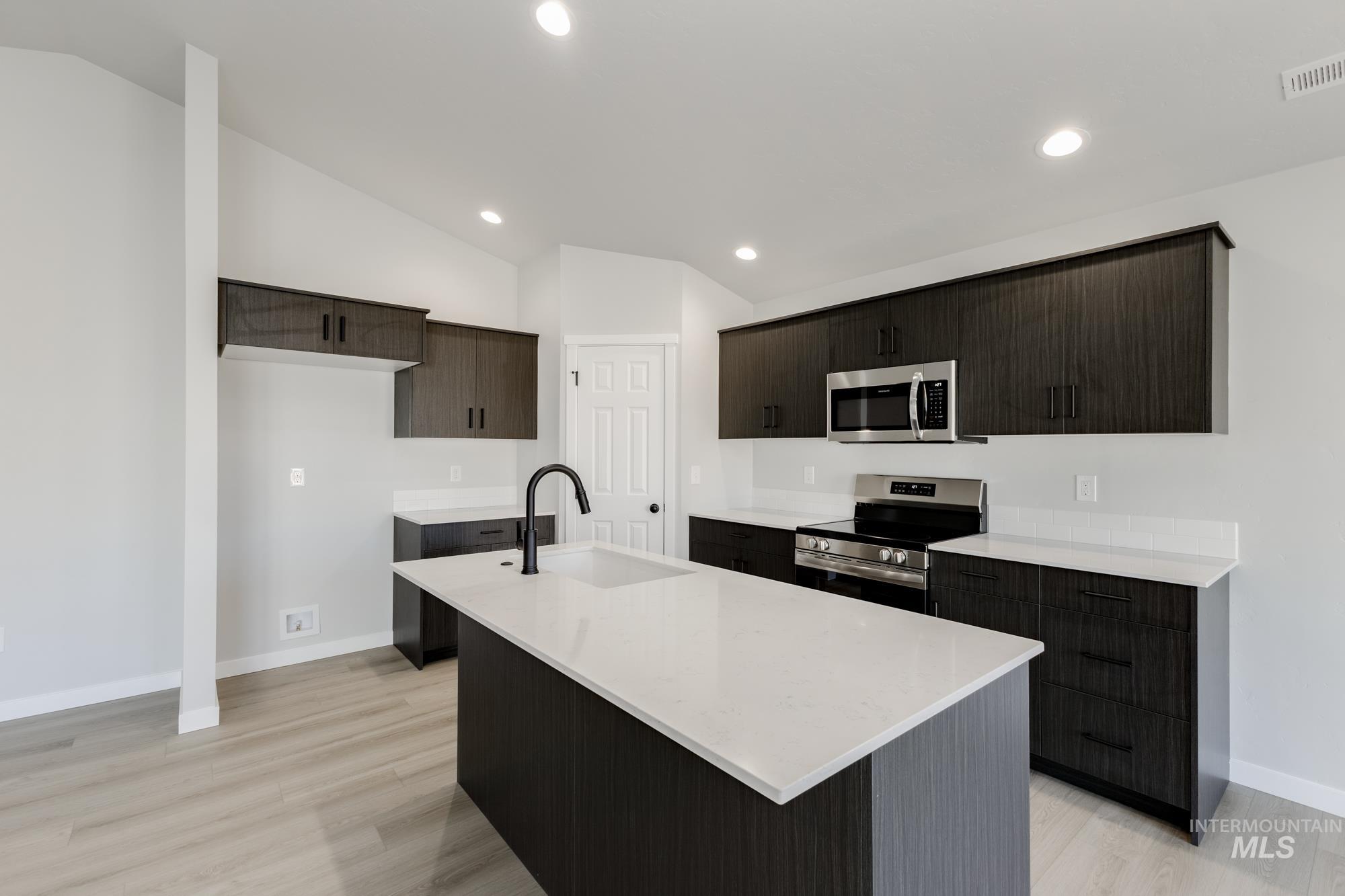 1804 West Unforgettable Street Meridian, ID 83642 - Photo 4 of 18 Kitchen featuring stainless steel appliances, vaulted ceiling, light stone counters, a center island with sink, and dark brown cabinetry