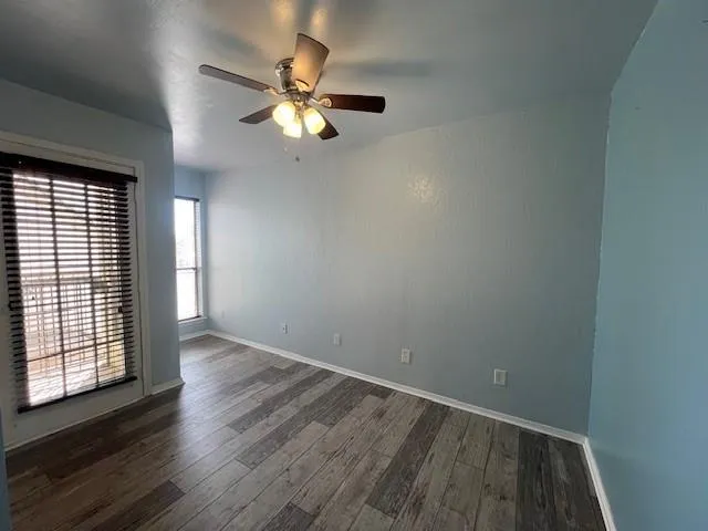 an empty room with wooden floor fan and windows