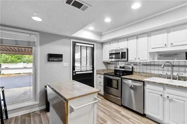 a kitchen with stainless steel appliances granite countertop a stove top oven a sink dishwasher a refrigerator and white cabinets with wooden floor