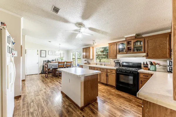 a kitchen with stainless steel appliances kitchen island granite countertop a stove top oven a sink a dining table and chairs with wooden floor