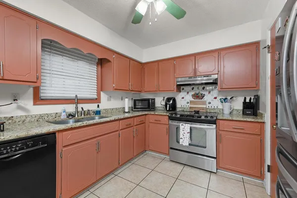 a kitchen with stainless steel appliances granite countertop a sink a stove a refrigerator cabinets and a window