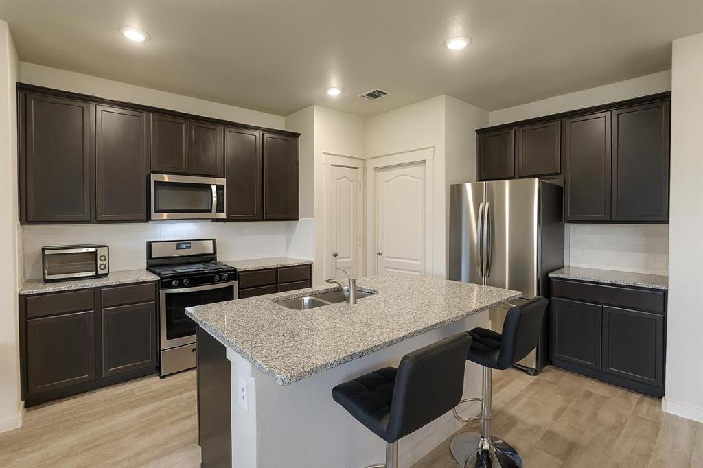 5641 Durst Lane Forney, TX 75126 - Photo 2 of 10 Kitchen with tasteful backsplash, appliances with stainless steel finishes, dark brown cabinetry, light stone countertops, and a kitchen breakfast bar