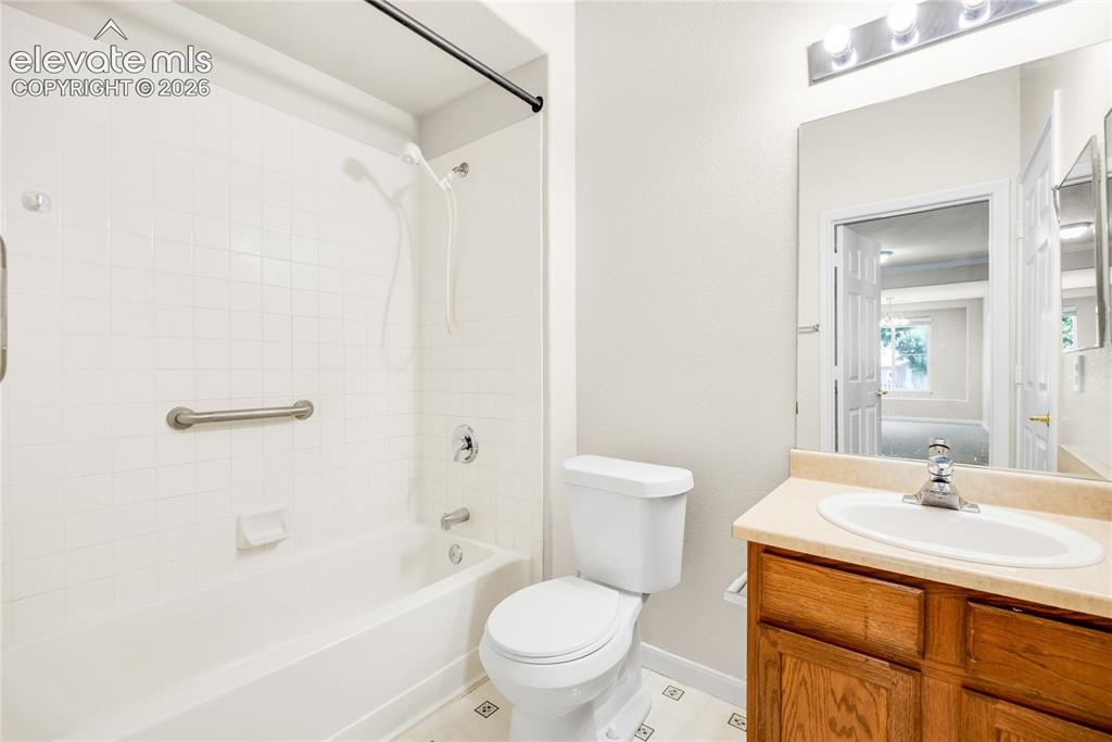 3864 Riviera Grove, Unit 102 Colorado Springs, CO 80922 - Photo 15 of 24 Bathroom featuring a white tiled shower-over-tub with grab bar, a wood-finish vanity with an integrated sink and light-toned countertop, and a built-in mirror with overhead lighting