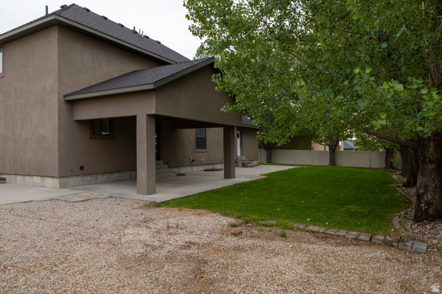 3565 West 1350th Street North Vernal, UT 84078 - Photo 53 of 54 Rear exterior featuring a covered patio, stucco siding, dark roof shingles, a gravel driveway, and a manicured lawn framed by mature trees