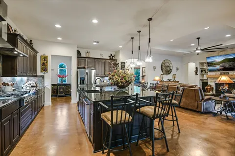 a kitchen with stainless steel appliances kitchen island granite countertop a stove top oven a sink a dining table and chairs with wooden floor