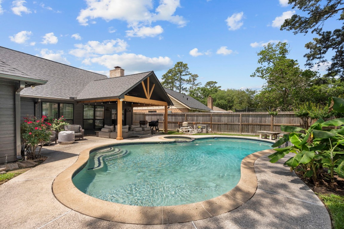 19602 Dianeshire Drive Spring, TX 77388 - Photo 36 of 37 Large backyard featuring a beautifully designed in-ground pool with a curved shape, surrounded by a landscaped patio. A covered seating area offers a perfect spot for relaxation, and mature trees provide added privacy.