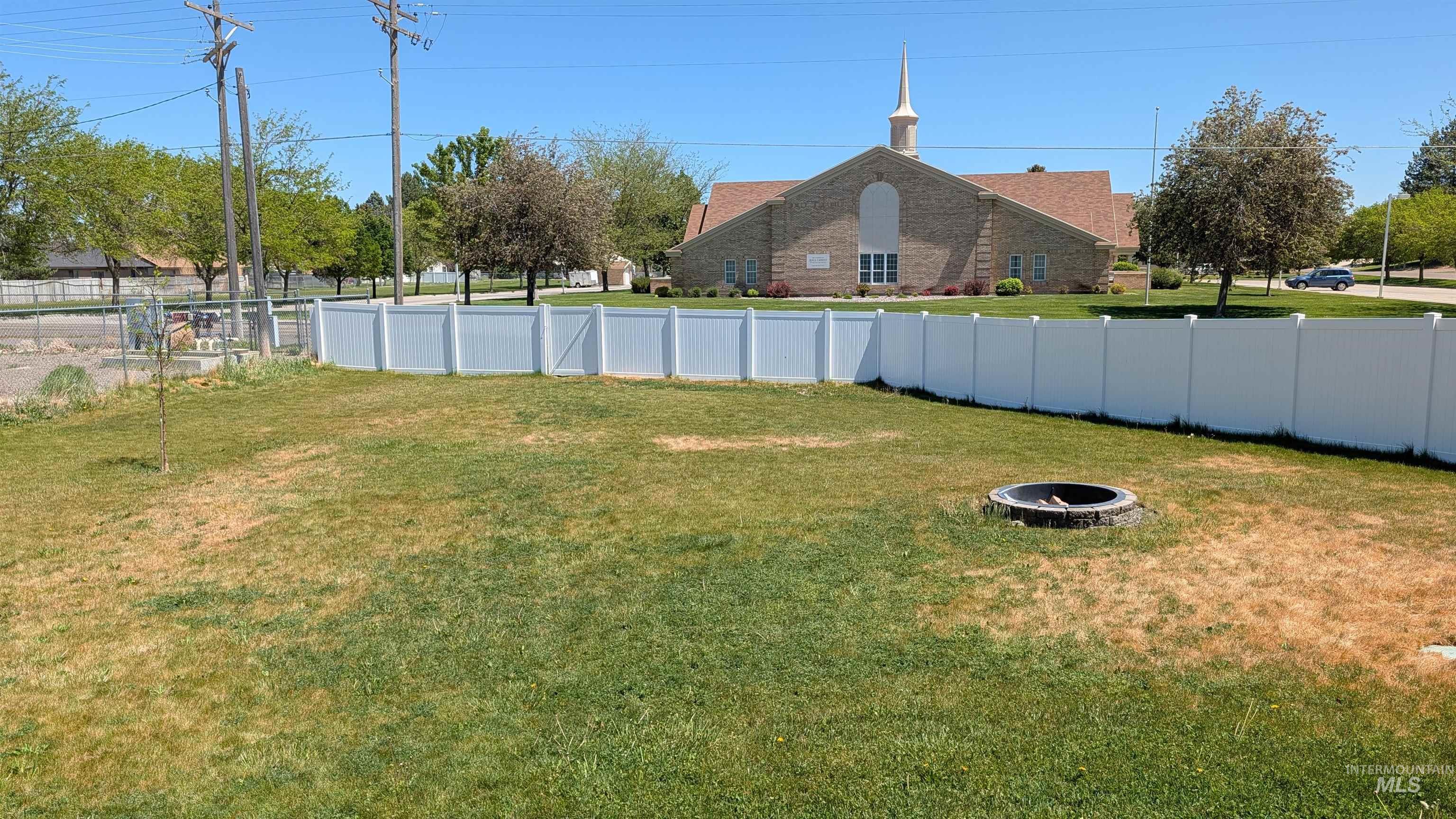 622 Lochsa Loop Heyburn, ID 83336 - Photo 16 of 17 Expansive grassy yard featuring a white vinyl privacy fence, a built-in fire pit, and mature perimeter trees