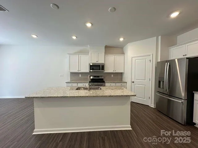 a kitchen with stainless steel appliances granite countertop a refrigerator a sink dishwasher a stove and white countertops with wooden floor