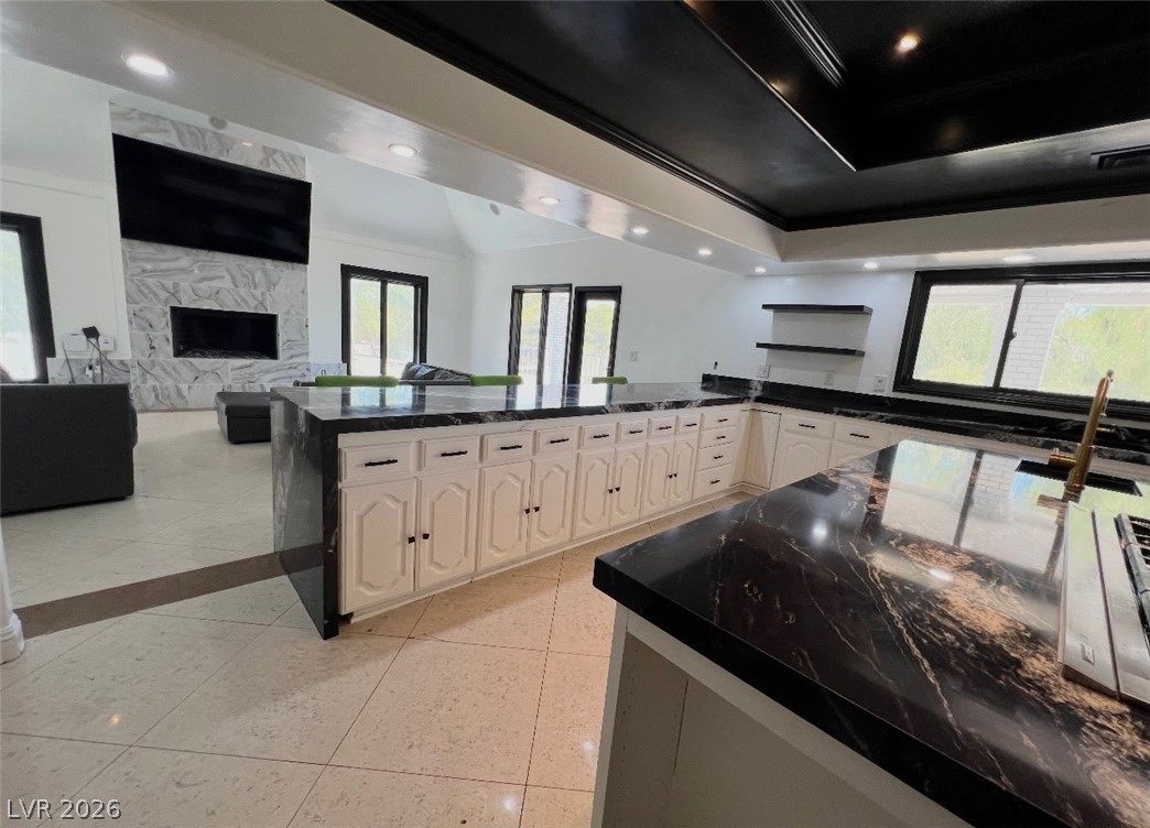 3003 Regency Hill Henderson, NV 89014 - Photo 5 of 13 A spacious kitchen with sleek black countertops flows into a living area featuring a striking marble fireplace.