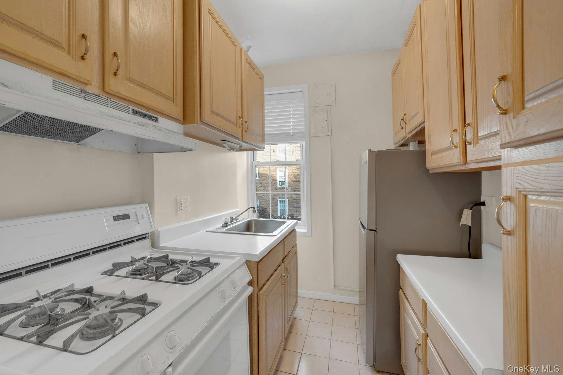 5 Midland Gardens, Unit 3M Bronxville, NY 10708 - Photo 13 of 19 Kitchen with white gas stove, light brown cabinetry, light countertops, light tile patterned floors, and under cabinet range hood