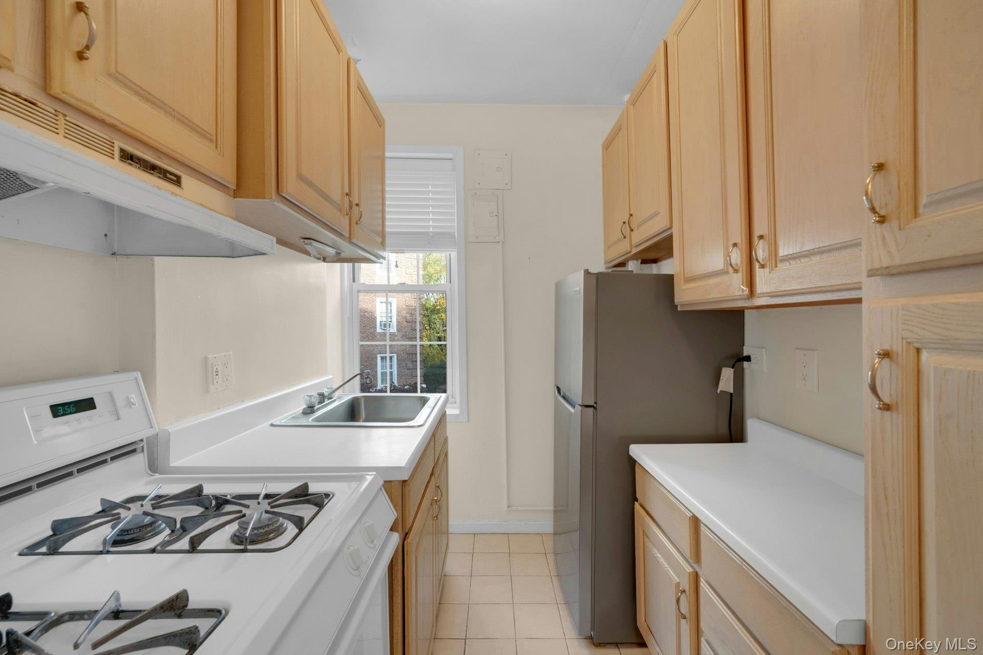 5 Midland Gardens, Unit 3M Bronxville, NY 10708 - Photo 14 of 19 Kitchen featuring light brown cabinetry, white gas stove, light countertops, light tile patterned floors, and freestanding refrigerator