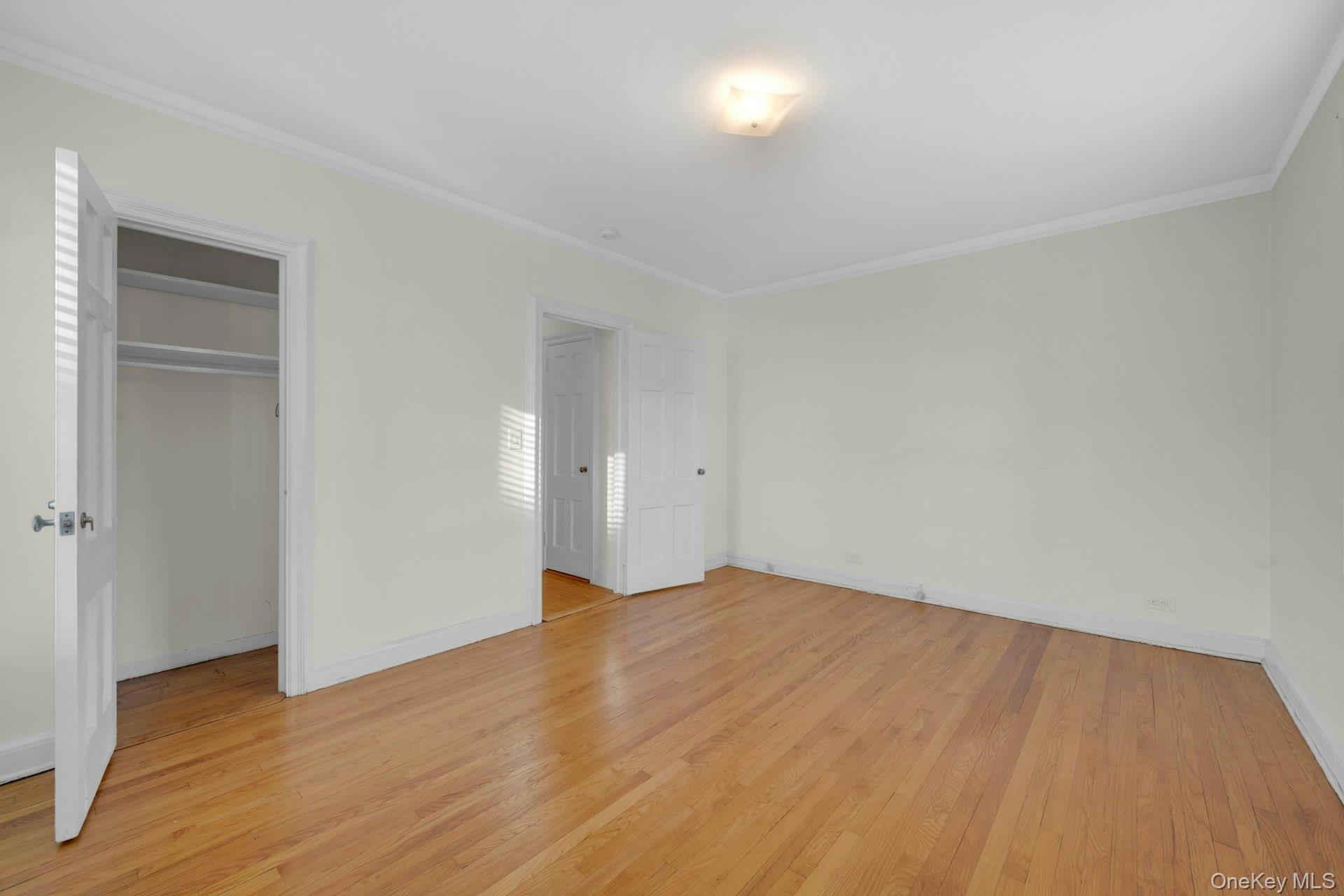 5 Midland Gardens, Unit 3M Bronxville, NY 10708 - Photo 17 of 19 Another view of the unfurnished primary bedroom featuring light wood-style flooring, ornamental molding, and a closet
