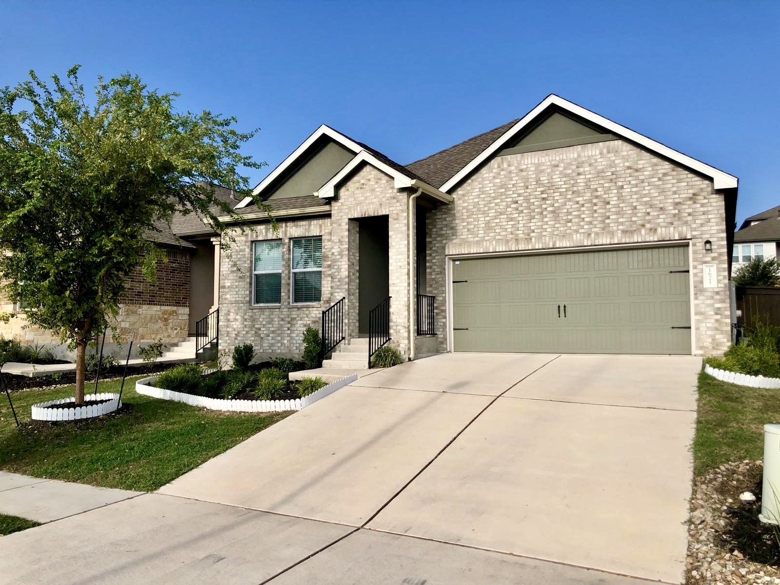 1621 Brueggerhoff Road Leander, TX 78641 - Photo 4 of 28 Contemporary brick exterior featuring a two-car garage, mature landscaping, concrete driveway, and front entry stairs with handrails