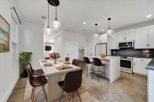 a kitchen with stainless steel appliances kitchen island granite countertop a dining table chairs and white cabinets
