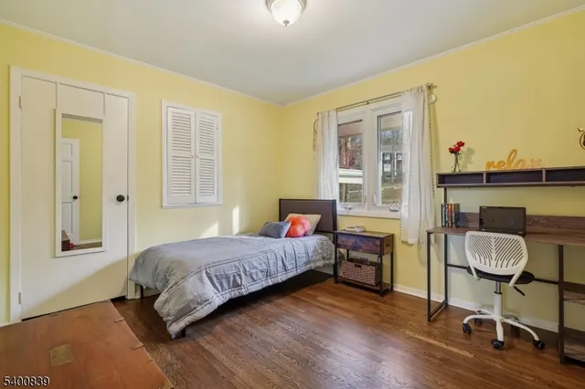 a bedroom with a bed a desk and chair with wooden floor