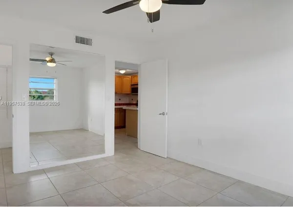 an empty room with chandelier fan and kitchen view