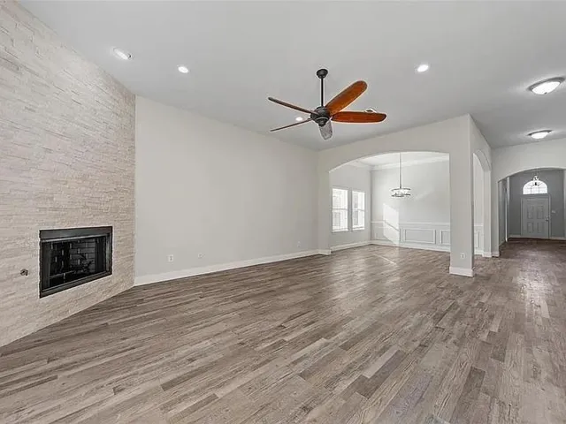 an empty room with wooden floor fireplace and a ceiling fan