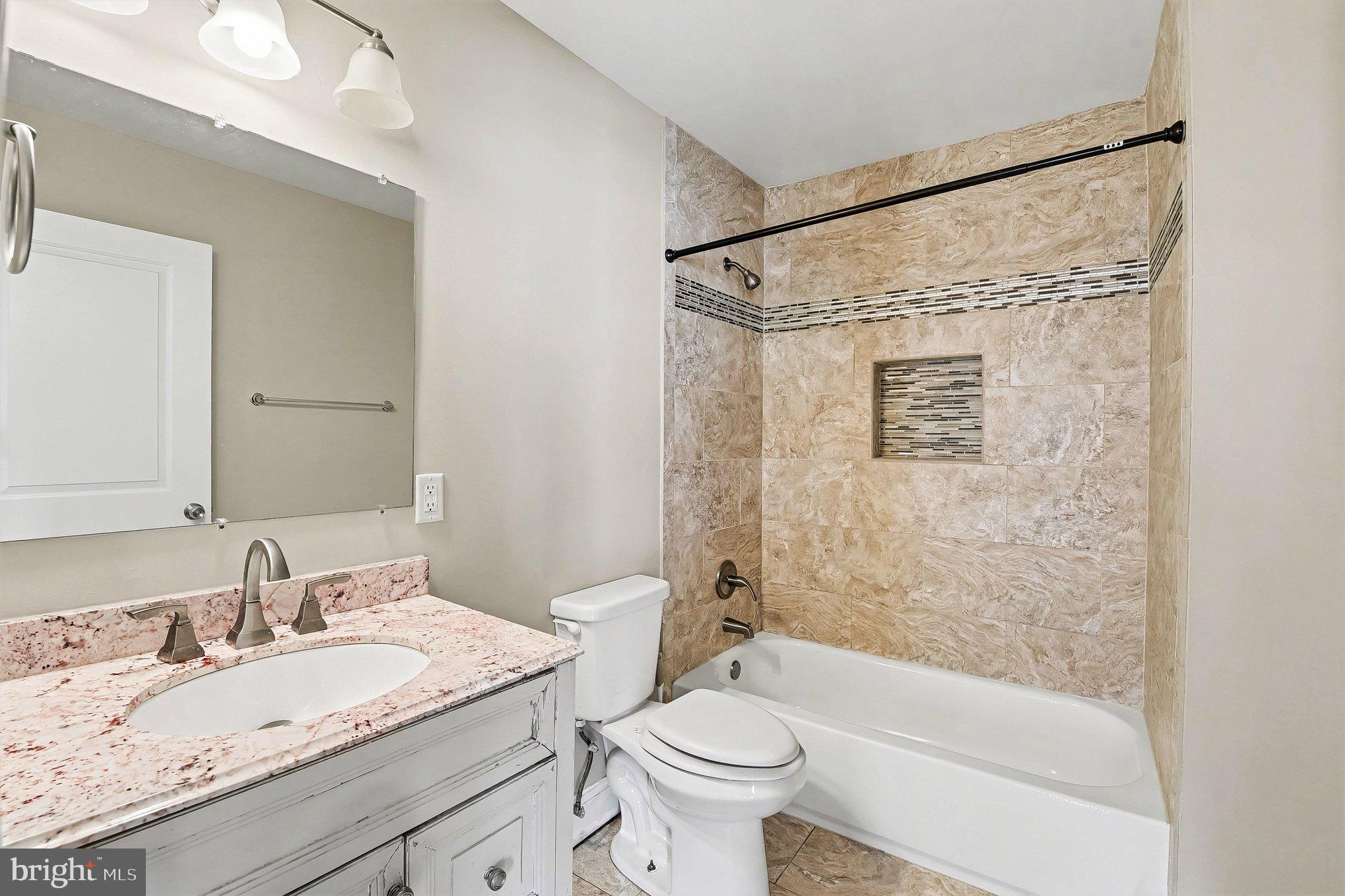 8716 Eddington Road Parkville, MD 21234 - Photo 9 of 27 a bathroom with a granite countertop sink a toilet a mirror a bathtub and shower