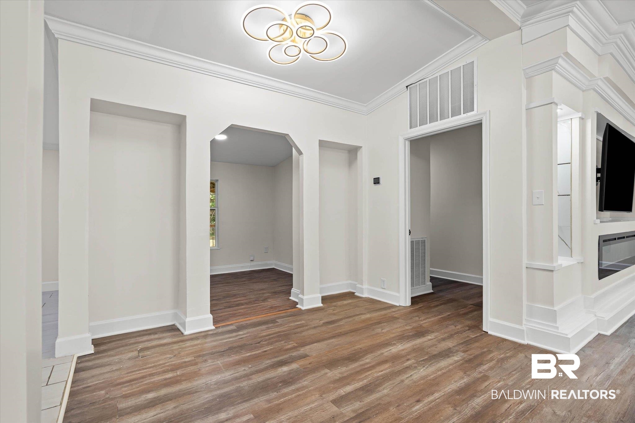 9230 McLeod Road Mobile, AL 36695 - Photo 6 of 20 Living area featuring wood-finish flooring, a contemporary ceiling light fixture, an arched doorway, and built-in shelving with an integrated media console