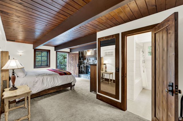 2983 East Ridgetop Road, Unit 27 Provo, UT 84604 - Photo 24 of 63 Carpeted sleeping quarters featuring a wood-plank ceiling with exposed beams, a built-in stone fireplace, wood-framed windows, and a private entryway to a bathroom with white tile flooring and a porcelain tub