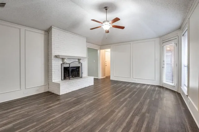 a view of an empty room with wooden floor fireplace and a window