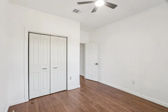an empty room with wooden floor closet and windows