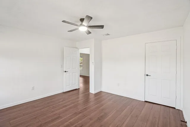 an empty room with wooden floor fan and windows