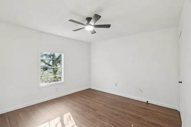an empty room with wooden floor fan and windows