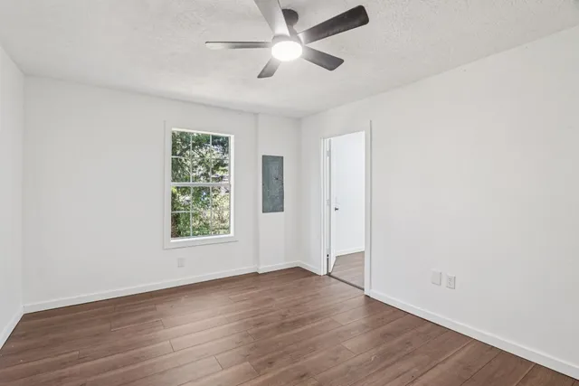 an empty room with wooden floor ceiling fan and windows