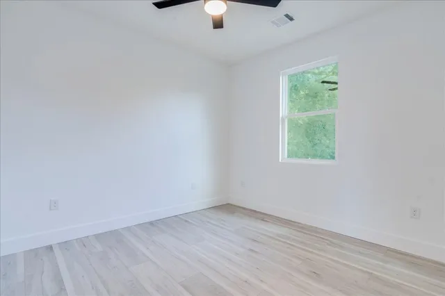 an empty room with wooden floor chandelier fan and windows