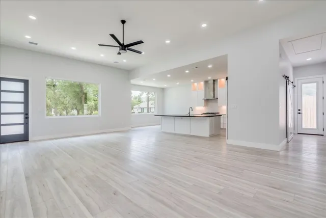 an empty room with wooden floor a ceiling fan and windows