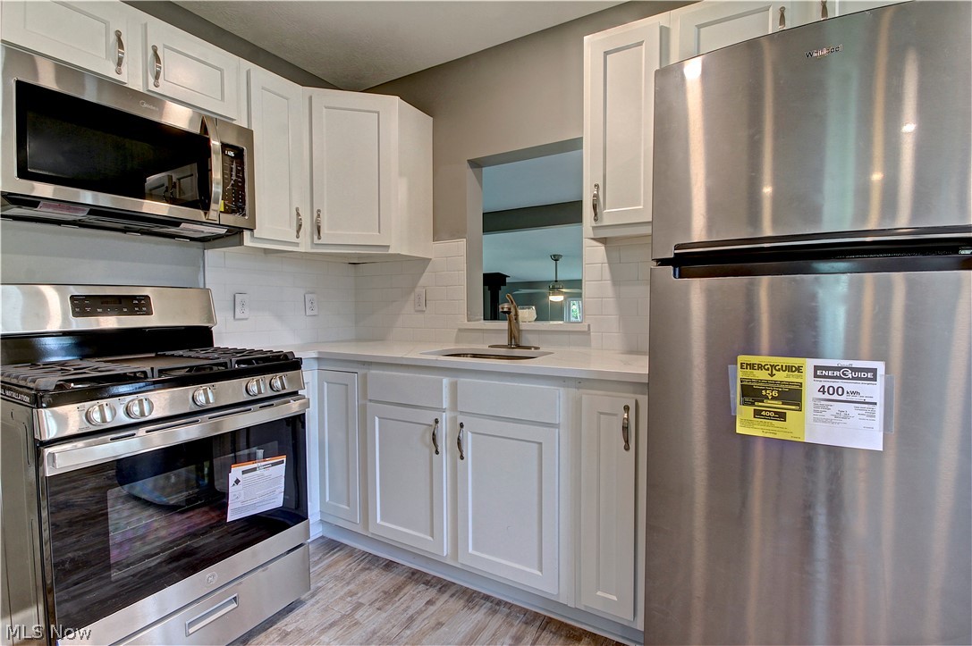14507 Glencliffe Road Cleveland, OH 44111 - Photo 12 of 31 Kitchen with backsplash, white cabinetry, light wood-type flooring, appliances with stainless steel finishes, and sink