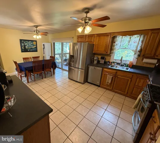 a kitchen with stainless steel appliances granite countertop a refrigerator a sink dishwasher a stove and a dining table with wooden floor