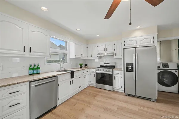 a kitchen with stainless steel appliances granite countertop a refrigerator a stove a sink and white cabinets with wooden floor
