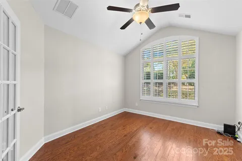 an empty room with wooden floor ceiling fan and windows